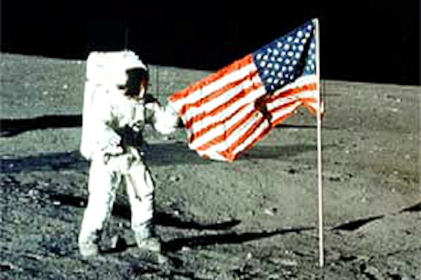 Neil Armstrong stands on the moon next to an American flag.