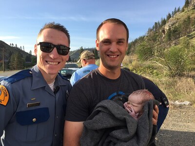 Senior Airman Travis Cunningham(left), 194th Intelligence Squadron, poses with a father and his newborn child near Winthrop, Wash., May 13, 2019. Cunningham, also a Washington State Trooper, helped deliver the baby on the side of the road after a traffic stop turned into a medical emergency.