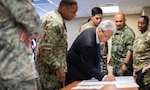 Group of people gather around man who is writing on paper.