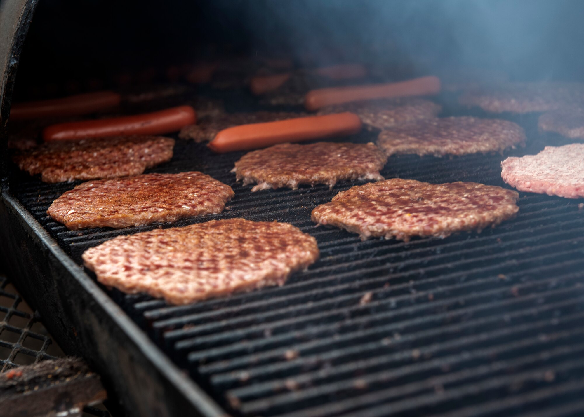 Burgers cook on a grill during the quarterly Committee of 100 dinner, July 8, 2019, at Altus, Okla. The dinner for this quarter’s military welcoming event consisted of burgers, hot links and hot dogs with snow cones offered after.