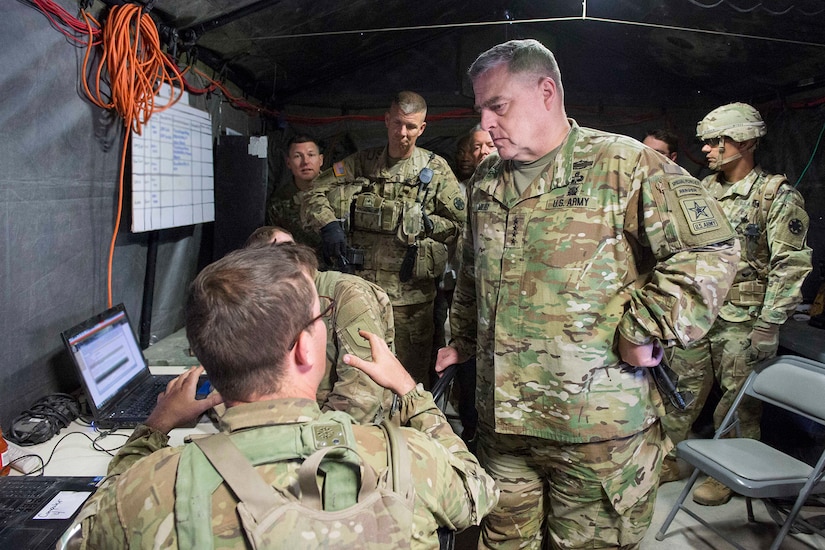 An Army officer speaks with  seated service members inside a tent.