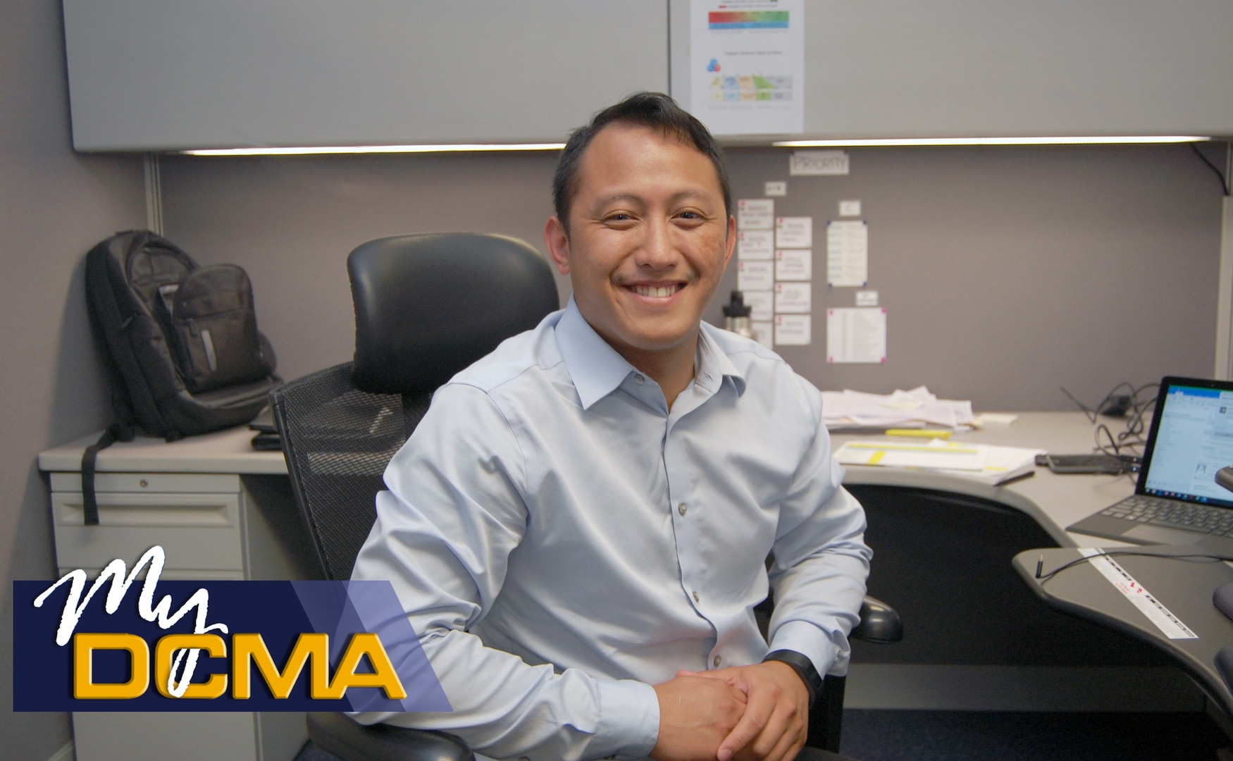 Smiling man sits in a chair in his cubicle