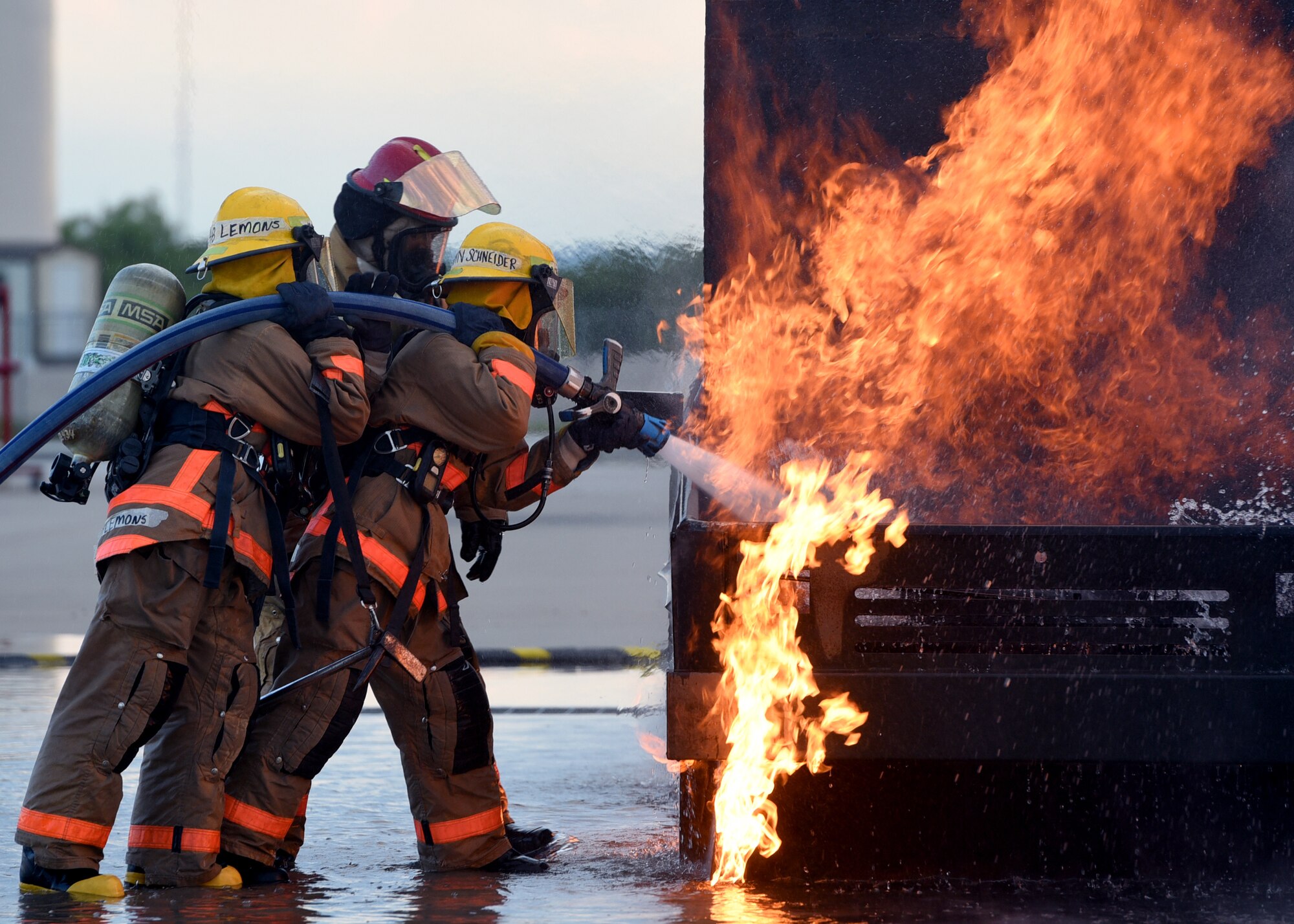 U.S. Air Force Airman Kristina Schneinder, 312th Training Squadron student, leads Airman Emalie Lemons, 312th TRS student, in a textbook style approach to a mock vehicle fire outside the Louis F. Garland Department of Defense Fire Academy on Goodfellow Air Force Base, Texas, July 11, 2019.  Schneinder and Lemons were trained in the classroom how to approach a live fire and what angle to spray the water hose for hood and undercarriage fires before their hands on experience. (U.S. Air Force Photo by Airman 1st Class Abbey Rieves/Released)