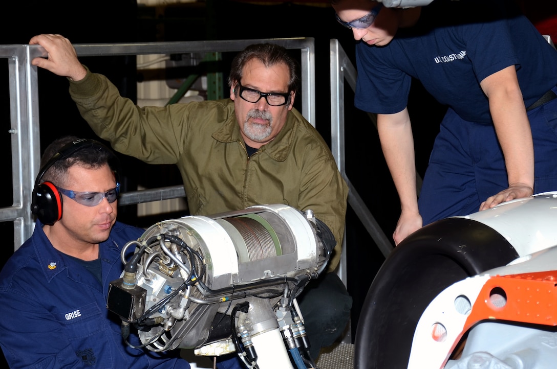 rthur Griffiths, a civilian instructor at the Coast Guard's Aviation Technical Training Center, teaches Petty Officer 2nd Class Gabriel E. Grise, of Goshen, Ind., how to perform maintenance on the rescue hoist of the MH-60 helicopter, while another student in advanced Aviation Maintenance Technician training observes March 18, 2014.