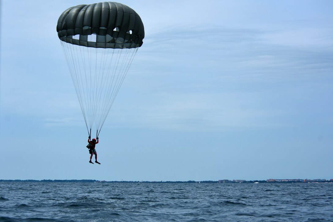 An airman wearing a parachutes descends into water.