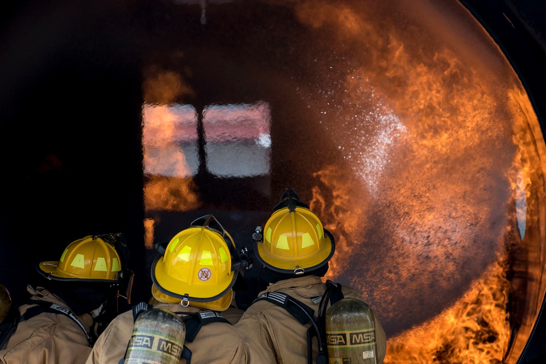 Firefighters battle a curving flame during training.