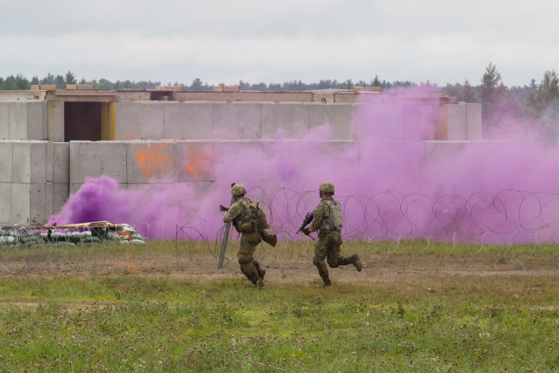 Two soldiers run toward the source of purple smoke during training.