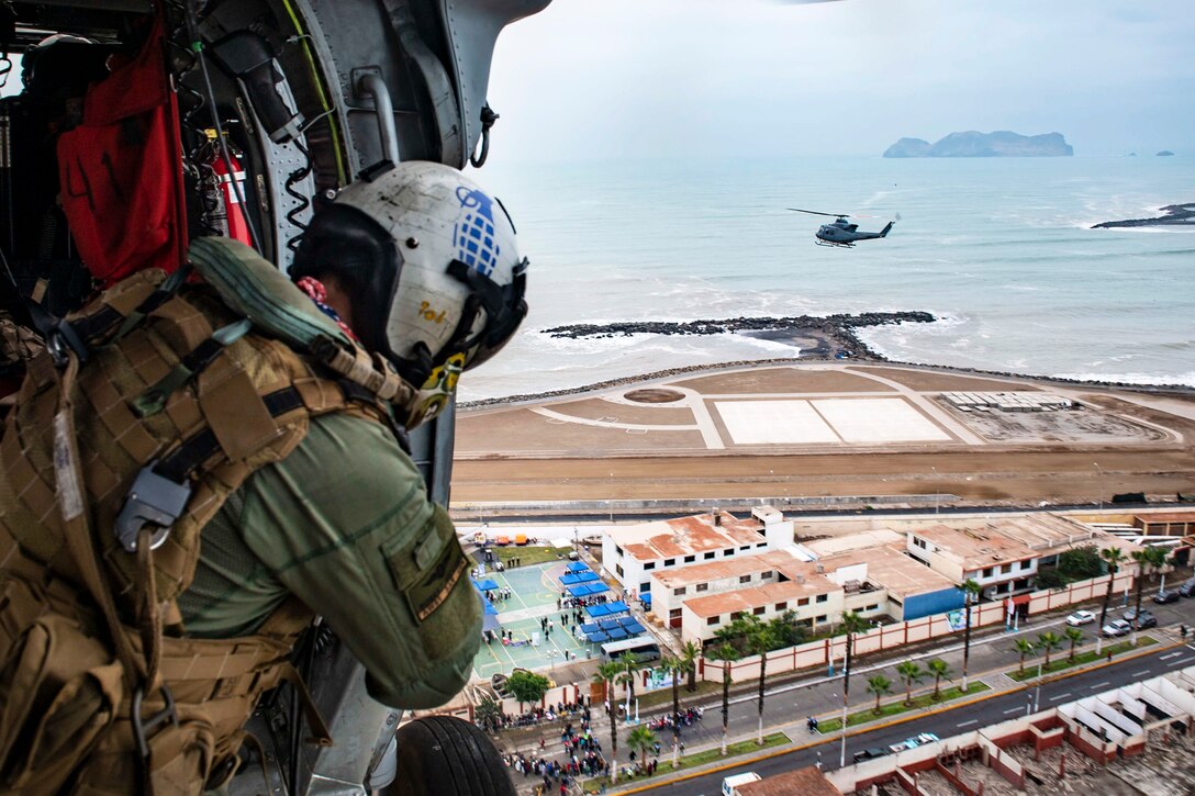 A sailor looks out over a site below from an airborne aircraft.