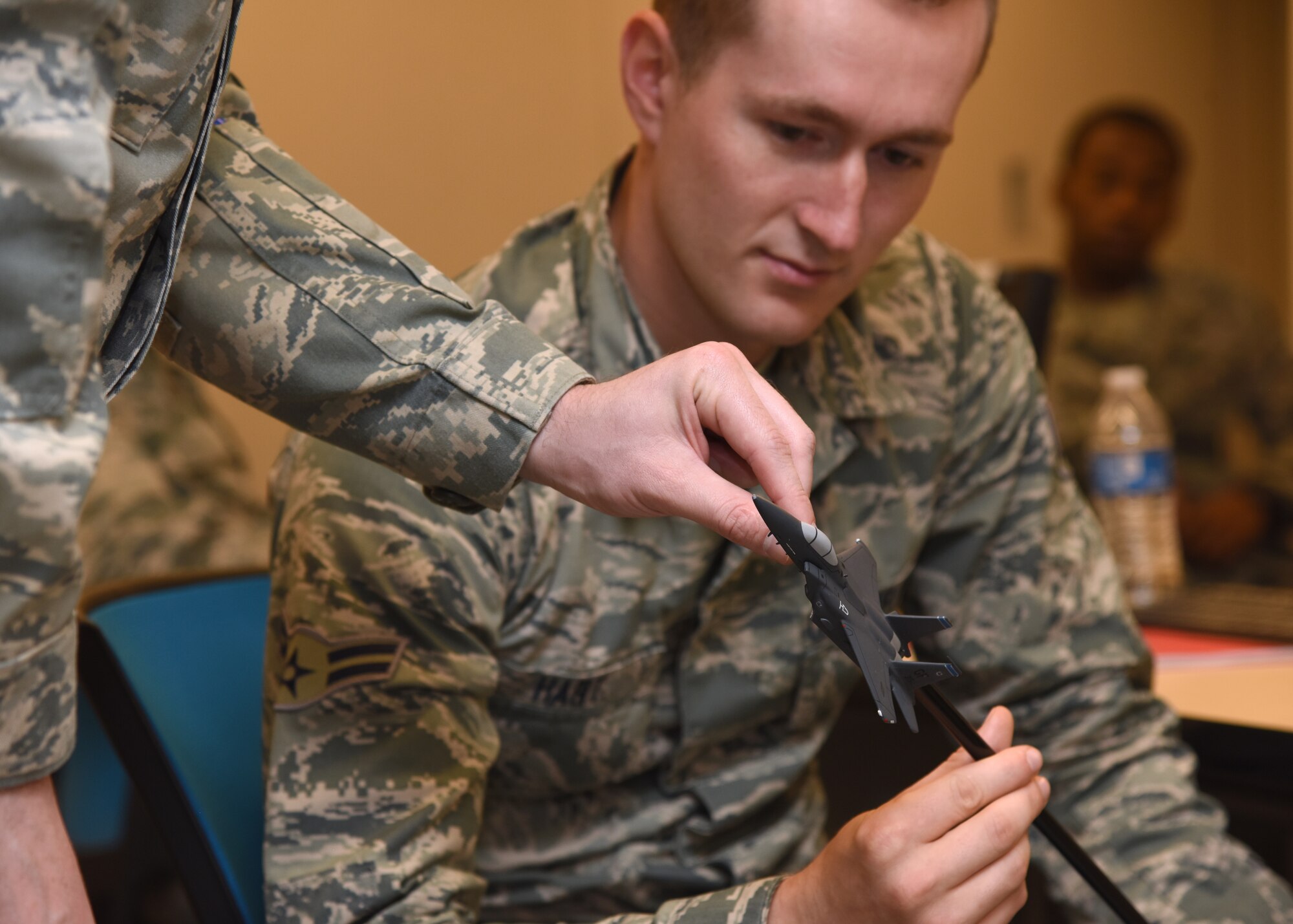 U.S. Air Force Airman 1st Class Neale Hart, 315th Training Squadron student, interacts with a miniature F-15E Strike Eagle aircraft prop as Staff Sgt. William McCauley, 315th TRS student, adjusts the proposed flying angle of the prop in Di Tommaso Hall on Goodfellow Air Force Base, Texas, July 10, 2019. Props are used in this classified learning environment to demonstrate larger-than-life concepts, which aid the students who learn visually. (U.S. Air Force photo by Airman 1st Class Abbey Rieves/Released)