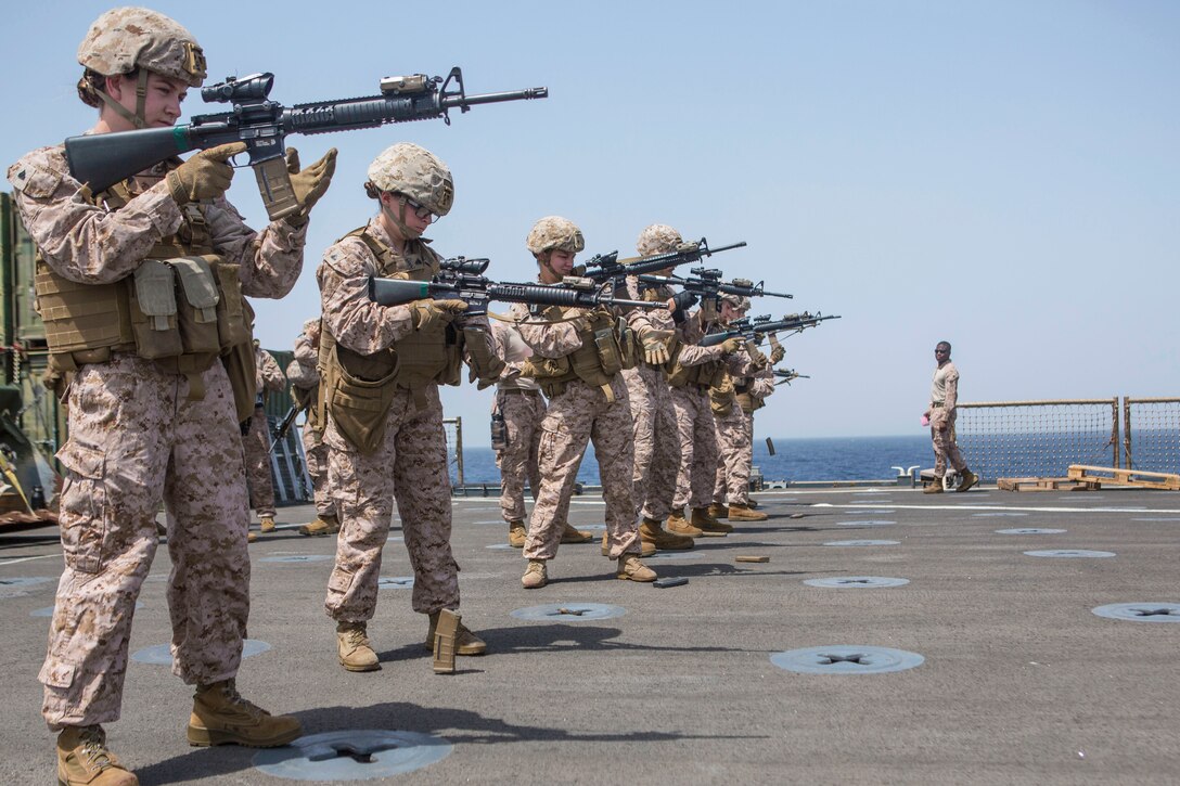 A groups of Marines and sailors load and aim weapons on deck of a ship.