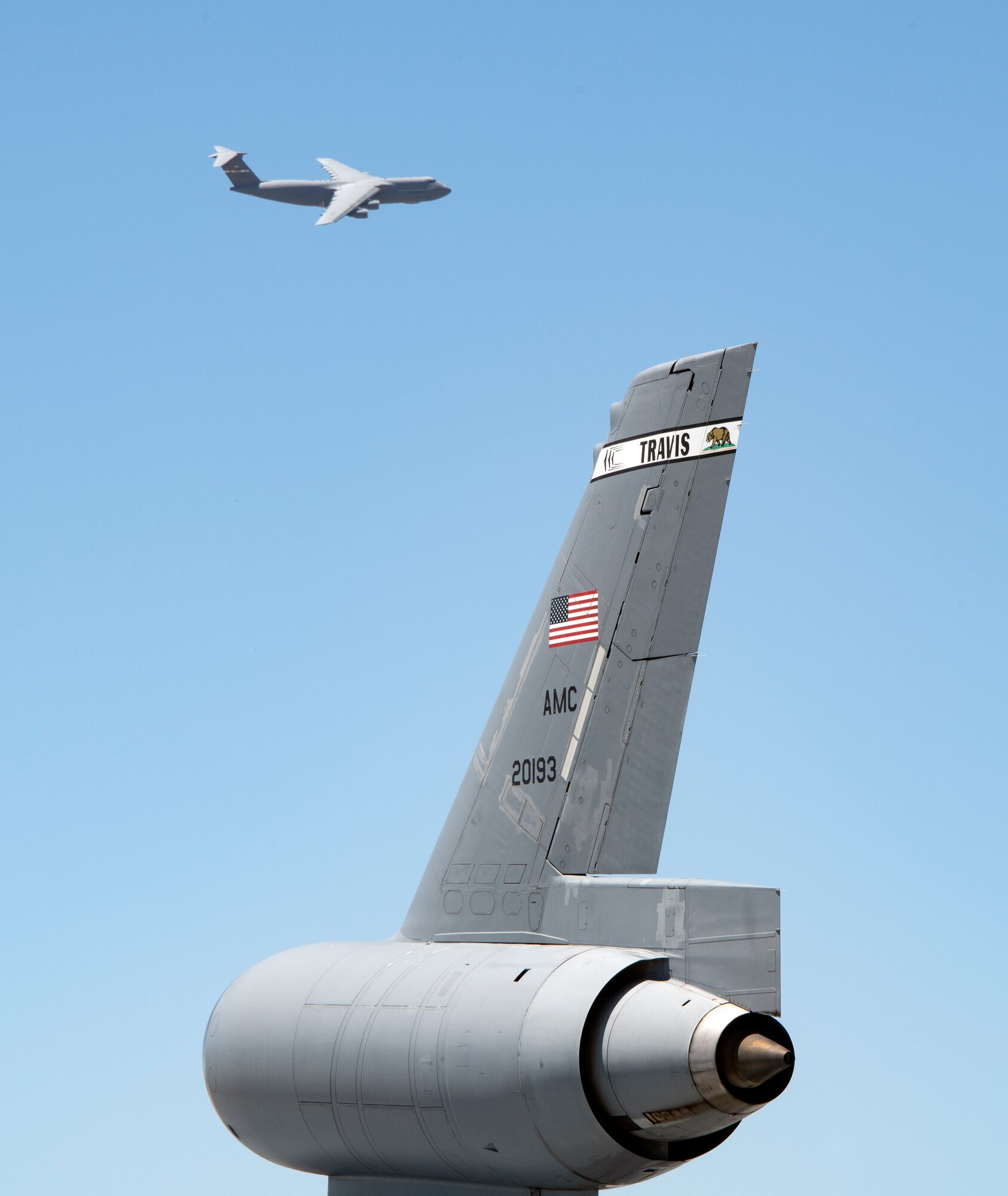 The tail of a KC-10 Extender is seen in the foreground of a departing C-5M Super Galaxy July 11, 2019, at Travis Air Force Base, California. With roughly 3,300 aircraft continuously arriving and departing on a monthly basis, Travis AFB handles more cargo and passenger traffic than any other military air terminal in the United States. (U.S. Air Force photo by Heide Couch)