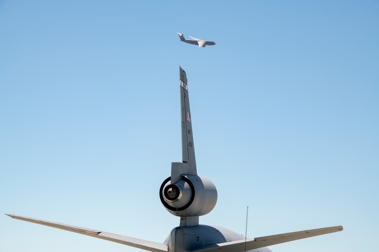 The tail of a KC-10 Extender is seen in the foreground of a departing C-5M Super Galaxy July 11, 2019, at Travis Air Force Base, California. With roughly 3,300 aircraft continuously arriving and departing on a monthly basis, Travis AFB handles more cargo and passenger traffic than any other military air terminal in the United States. (U.S. Air Force photo by Heide Couch)