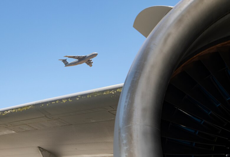 The engine of a KC-10 Extender is seen in the foreground of a departing C-5M Super Galaxy July 11, 2019, at Travis Air Force Base, California. With roughly 3,300 aircraft continuously arriving and departing on a monthly basis, Travis handles more cargo and passenger traffic than any other military air terminal in the United States. (U.S. Air Force photo by Heide Couch)
