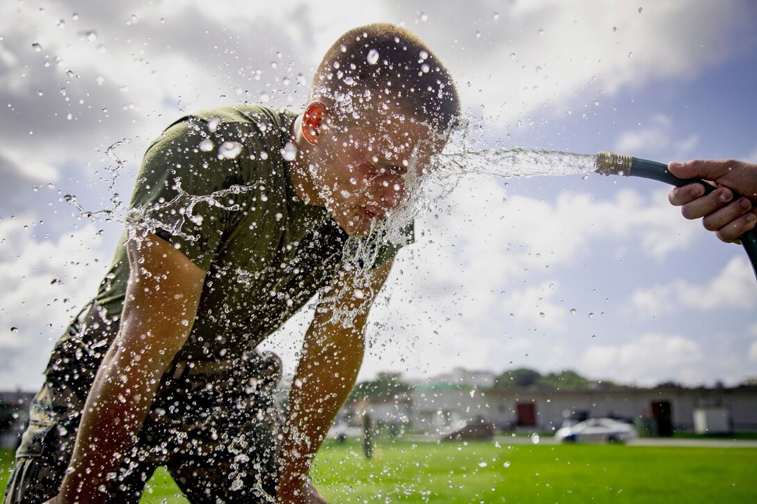 A sailor gets sprayed in the face with water from a person holding a water hose.