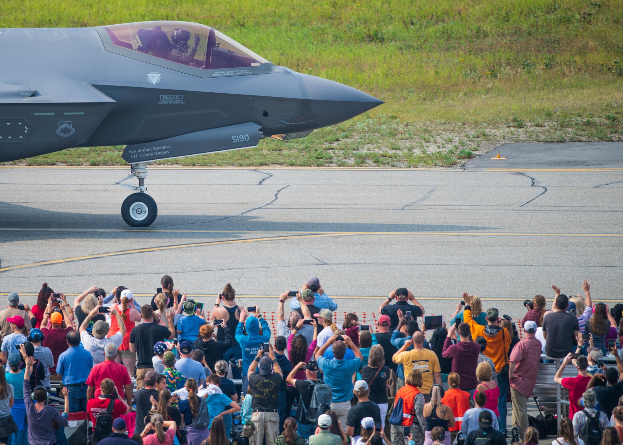 Airshow spectators wave as Capt. Andrew “Dojo” Olson, F-35 Demonstration Team pilot and commander returns from performing an aerial demonstration during the Arctic Lightning Airshow July 13, 2019, at Eielson Air Force Base, Alaska. Spectators got an up-close look at the Air Force’s newest fighter jet marking the airshow since 2008. (U.S. Air Force photo by Senior Airman Alexander Cook)