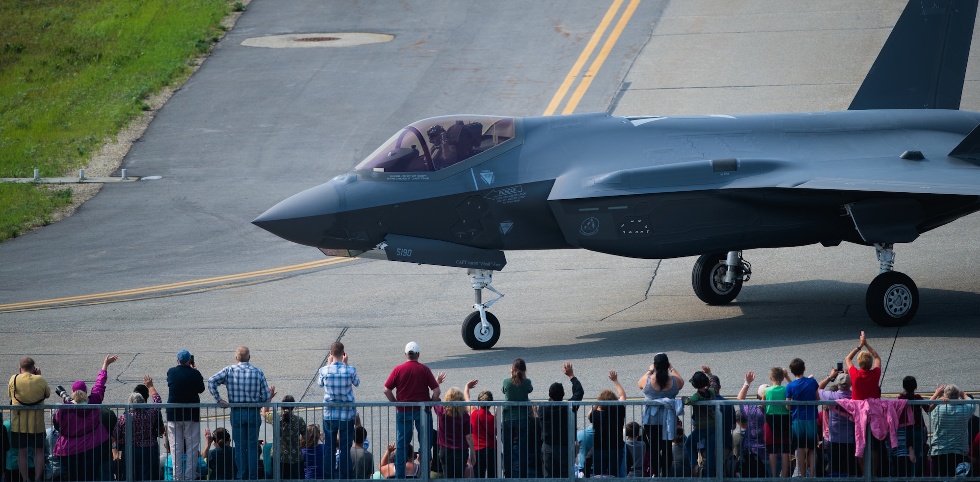 Airshow spectators wave as Capt. Andrew “Dojo”Olson, F-35 Demonstration Team pilot and commander returns from performing an aerial demonstration during the Arctic Lightning Airshow July 13, 2019, at Eielson Air Force Base, Alaska. Spectators got an up-close look at the Air Force’s newest fighter jet marking the airshow since 2008. (U.S. Air Force photo by Senior Airman Alexander Cook)