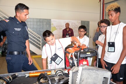 Raymundo Parraguirre, 802nd Civil Engineer Squadron firefighter, talks with students with the San Antonio Chapter of Tuskegee Airmen Inc.’s Youth Science, Technology, Engineering and Mathematics-Aviation Program about firefighter tools during a tour of Fire Station No. 1 at Joint Base San Antonio-Lackland July 12.