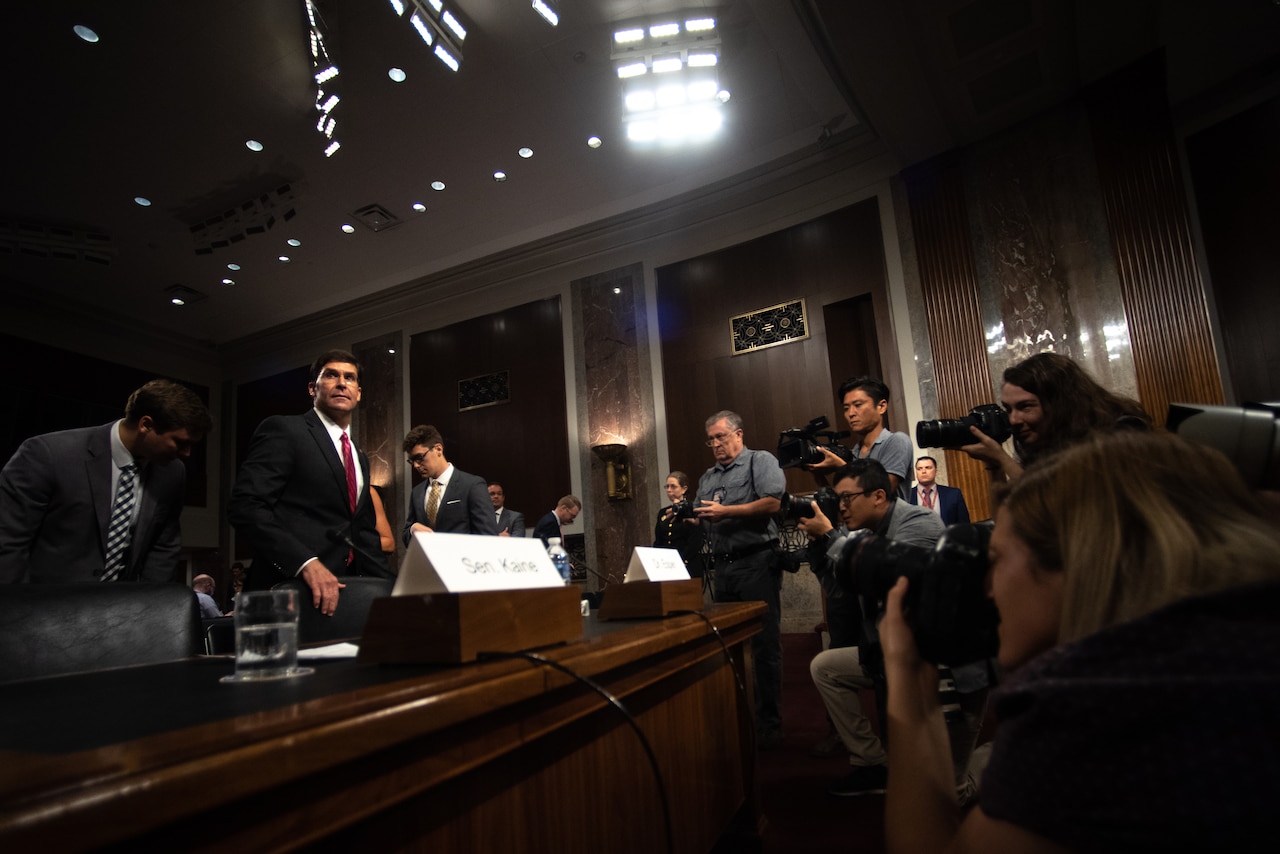 Man prepares to sit at a table as photographers take his picture.