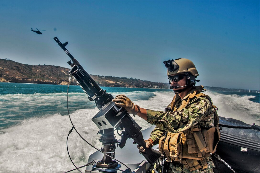 A sailor stands on a boat hold a weapon upright.