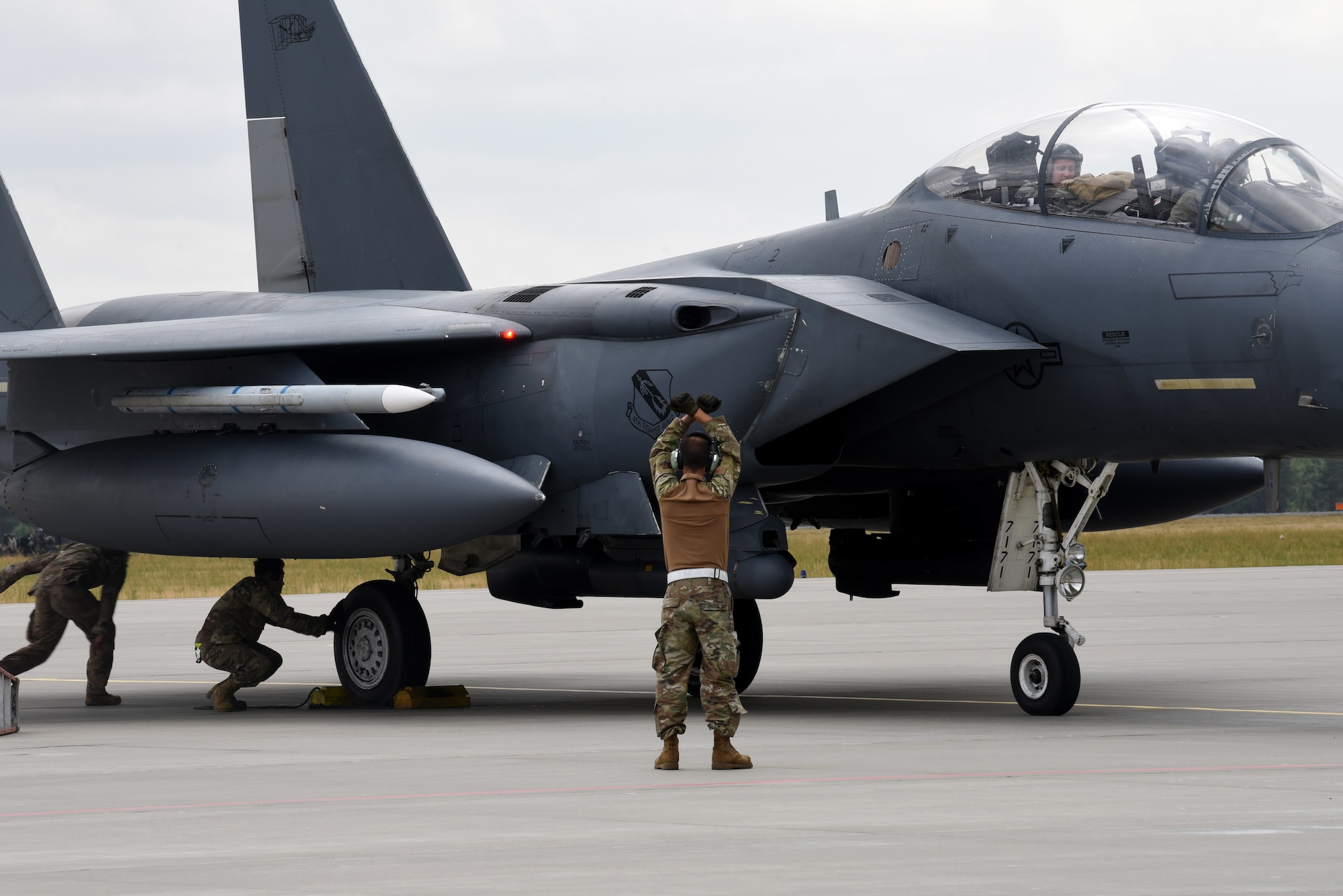 A U.S. Air Force member from the 336th Fighter Squadron, 4th Fighter Wing, Seymour Johnson Air Force Base, N.C., gives taxi instructions to an F-15 Strike Eagle fighter jet pilot during Operation Rapid Forge on Powidz Air Base, Poland, July, 16, 2019. Operation Rapid Forge is intended to enhance interoperability with NATO allies to improve combined operational capabilities.