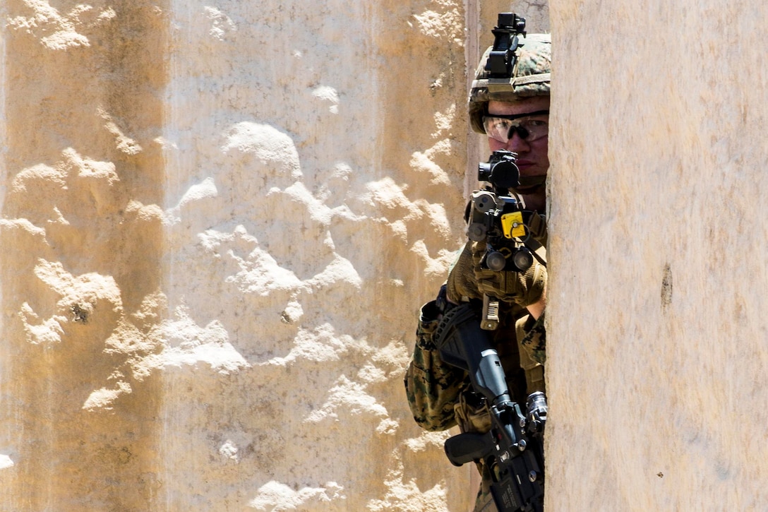 A Marine stands behind a wall while holding a rifle.