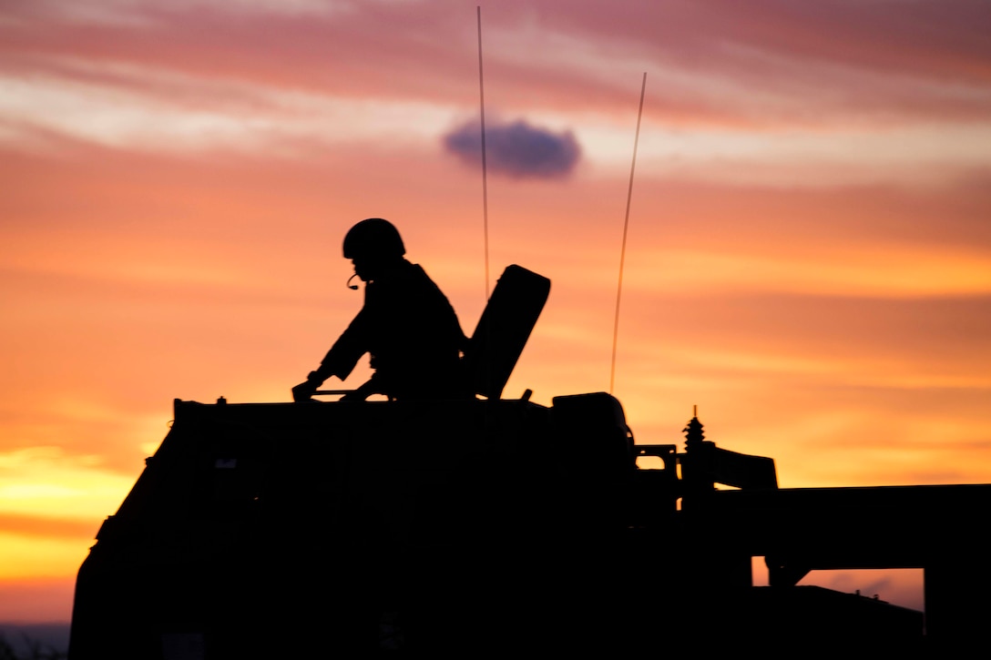 A silhouette of a Marine on top of a military vehicle.