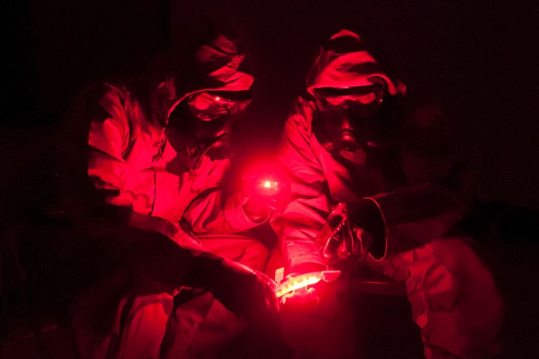 Two soldiers hold a device that is emanating red light.