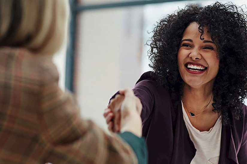 Woman facing camera shakes hands with woman facing her.