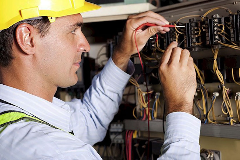 Electrician works on circuit panel.