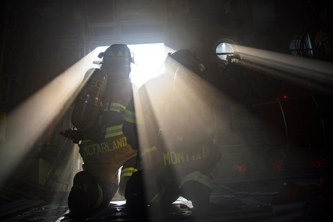 Two airmen kneeling in front of a small aircraft window with light shining through.