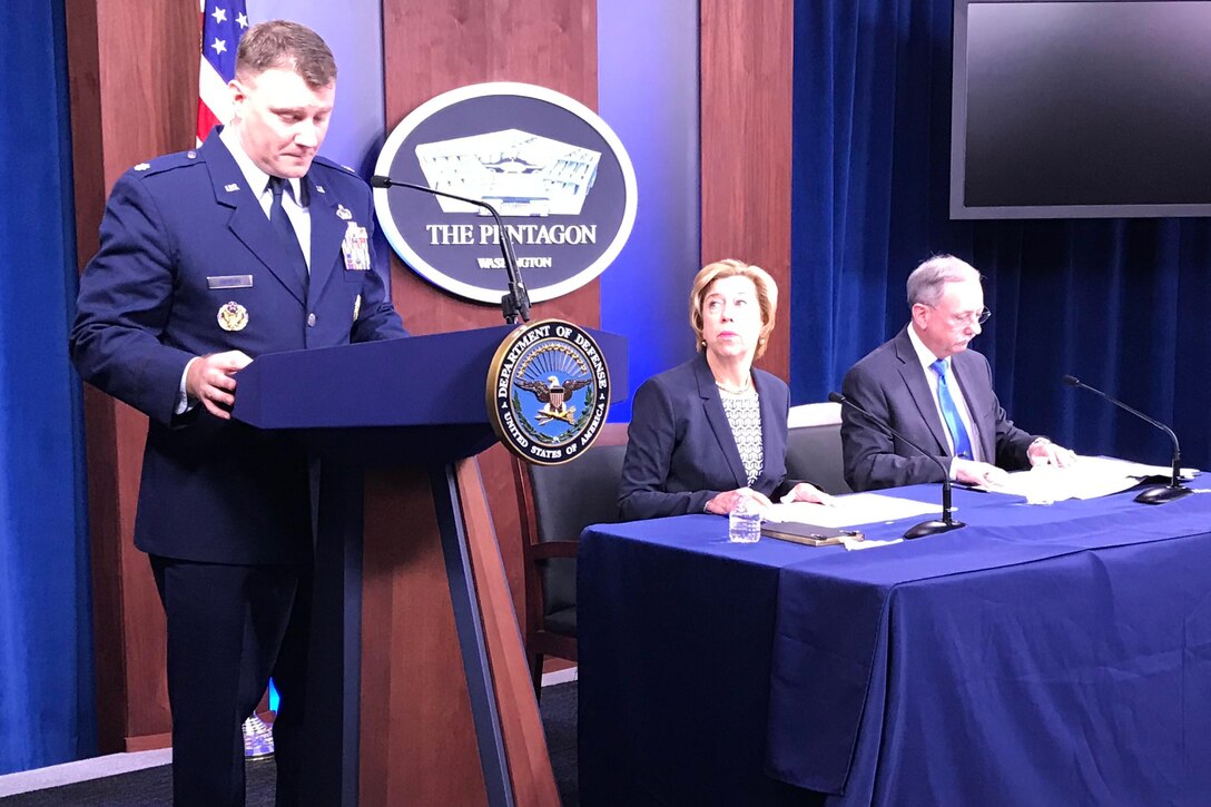 Service member at podium, DOD officials sitting at table.