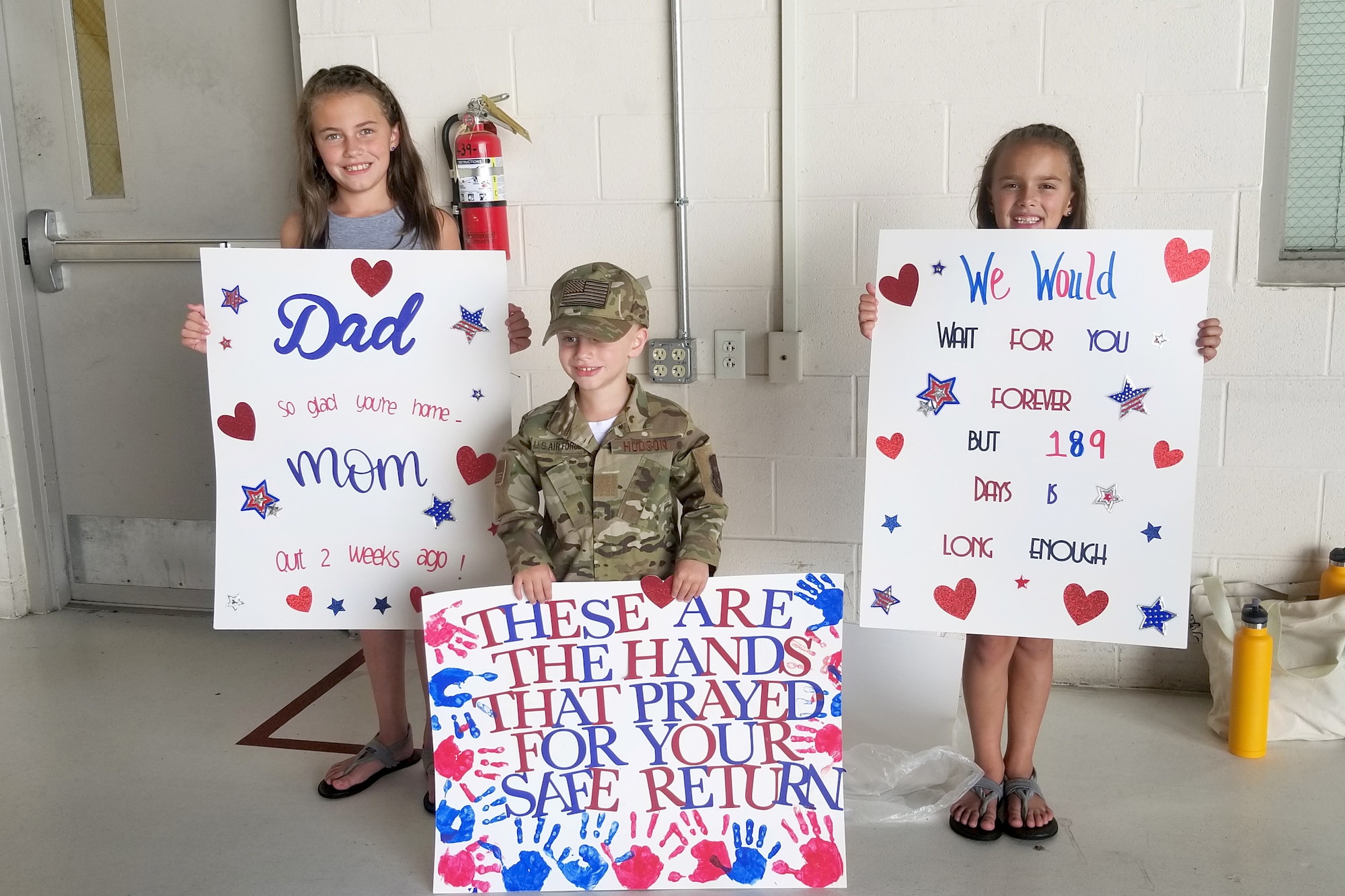 Charlee, Hudson and Mila Morris pose with signs July 15, 2019 at Grissom Air Reserve Base, Indiana while waiting for their father, Master Sgt. Michael Morris, to return home from his deployment. Their father along with 15 other Airmen were greeted and flown home by leadership after arriving at the Baltimore-Washington International airport. (U.S. photo/Ben Mota)
