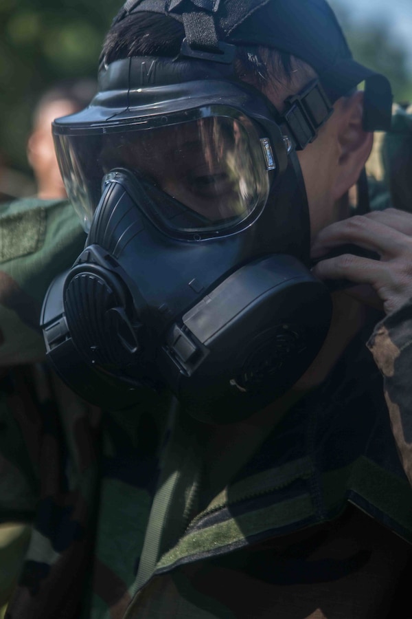 U.S. Marine Corps Lance Cpl. Brian Nguyen, a digital wideband repairman with Marine Wing Communications Squadron 48, Marine Air Control Group 48, 4th Marine Aircraft Wing, demonstrates how to put on a gas mask at Joliet Army Training Area, Elwood, Ill., July 15, 2019. MWCS-48 is conducting exercises ranging from rifle and pistol qualifications to land navigation to meet annual training requirements, as well as increase occupational proficiency. (U.S. Marine Corps photo by Lance Cpl. Preston L. Morris)