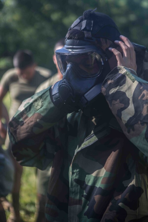 U.S. Marine Corps Lance Cpl. Brian Nguyen, a digital wideband repairman with Marine Wing Communications Squadron 48, Marine Air Control Group 48, 4th Marine Aircraft Wing, demonstrates how to put on a gas mask at Joliet Army Training Area, Elwood, Ill., July 15, 2019.  MWCS-48 is conducting exercises ranging from rifle and pistol qualifications to land navigation to meet annual training requirements, as well as increase occupational proficiency. (U.S. Marine Corps photo by Lance Cpl. Preston L. Morris)