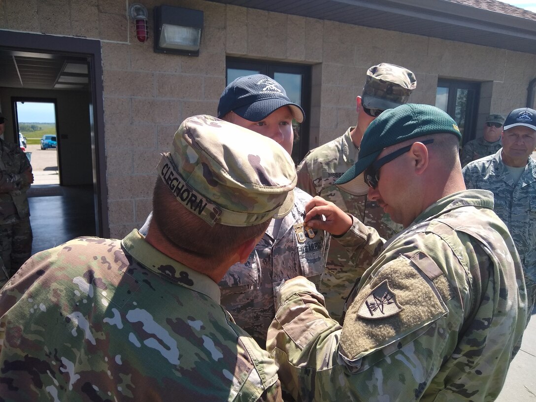 Lt. Col. Ben Cleghorn and Sgt. Andrew Maley, of the 817th Engineer Company, pin Distinguished Marksmanship Badges on the uniform of Senior Airman Gavin Rook, of the 119th Wing, at the 2019 North Dakota National Guard Adjutant General's Combat Marksmanship Match at the Camp Grafton Training Center firing complex, near McHenry, North Dakota, July 14, 2019.