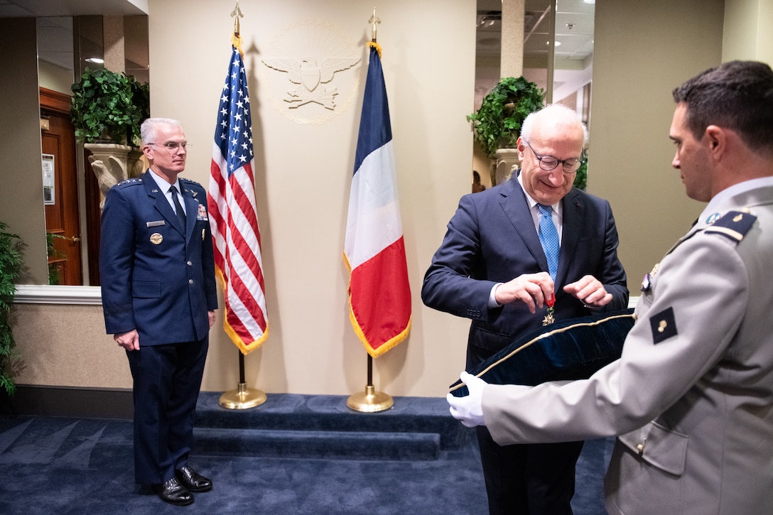 A man picks up a medal off a pillow while a decorated airman stands ready to receive the award.