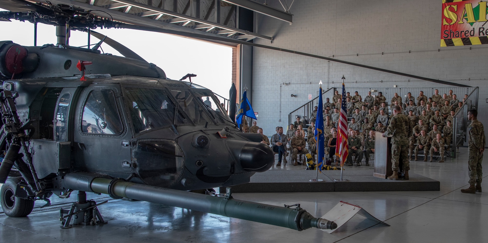 A crowd sits behind a helicopter during a ceremony.