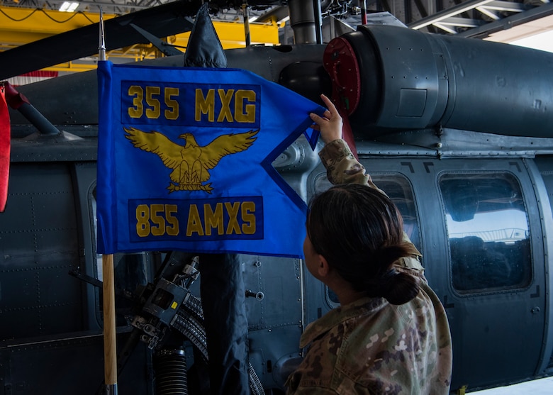 An Airman straightens a guidon flag in front of a helicopter.