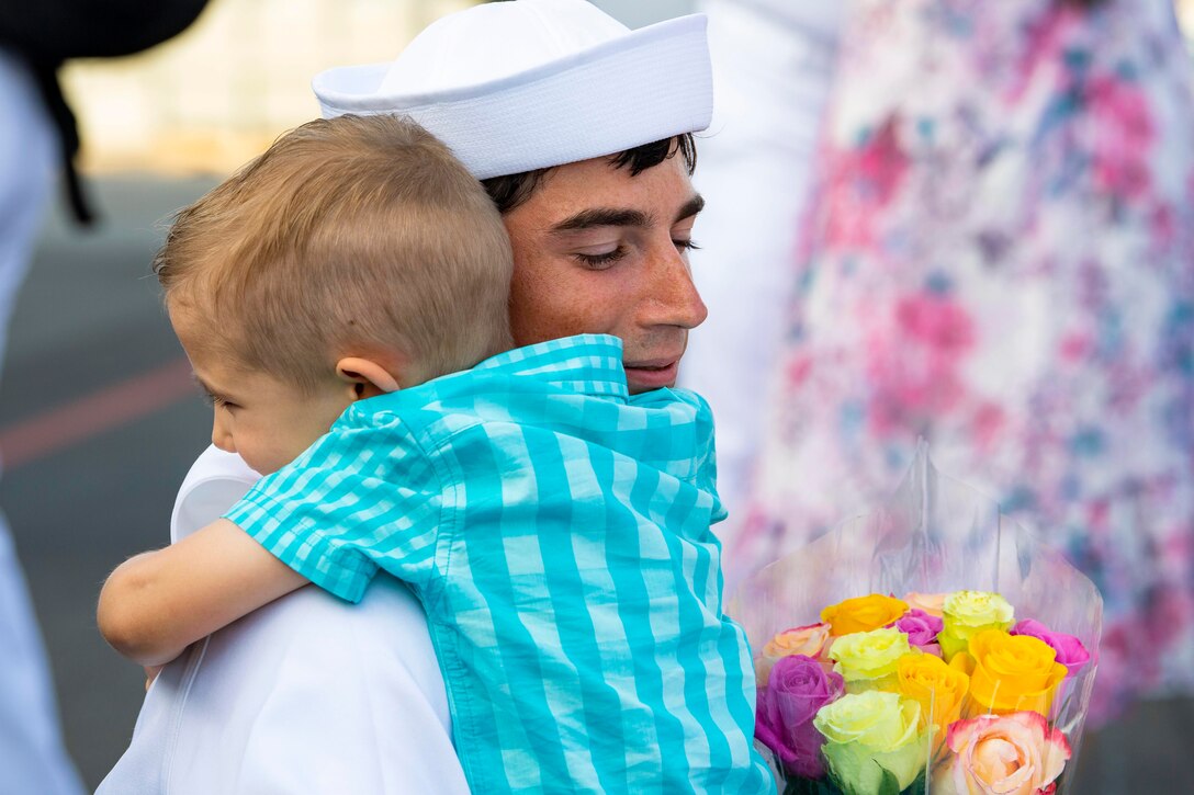 A sailor hugs a child.