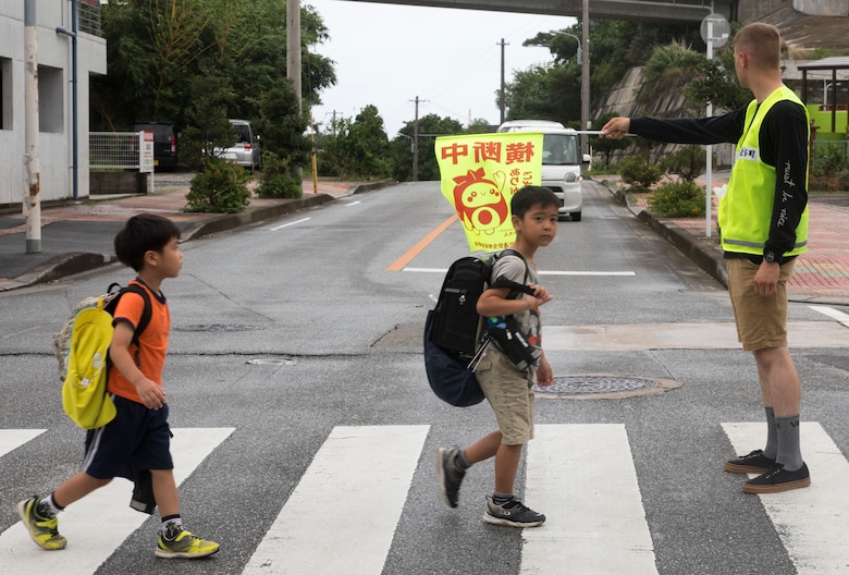 U.S. Marine Corps Lance Cpl. Timothy Silva guides local elementary school children through a crosswalk July 18, 2019. Crossing guard duty is one of the multiple roles conducted by volunteer Marines on camp guard duty.