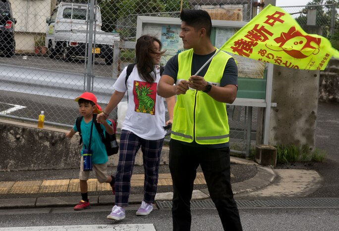 U.S. Marine Corps Pfc. Alfonso Padilla, guides a local elementary school child and his mother at a crosswalk July 18, 2019. Crossing guard duty is one of the multiple tasks conducted by Marine volunteers on Okinawa.