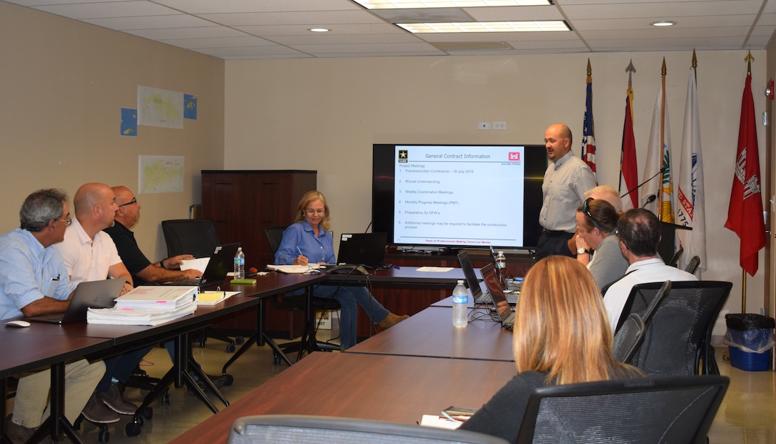 Eight people seating around a conference room table and a presenter standing.