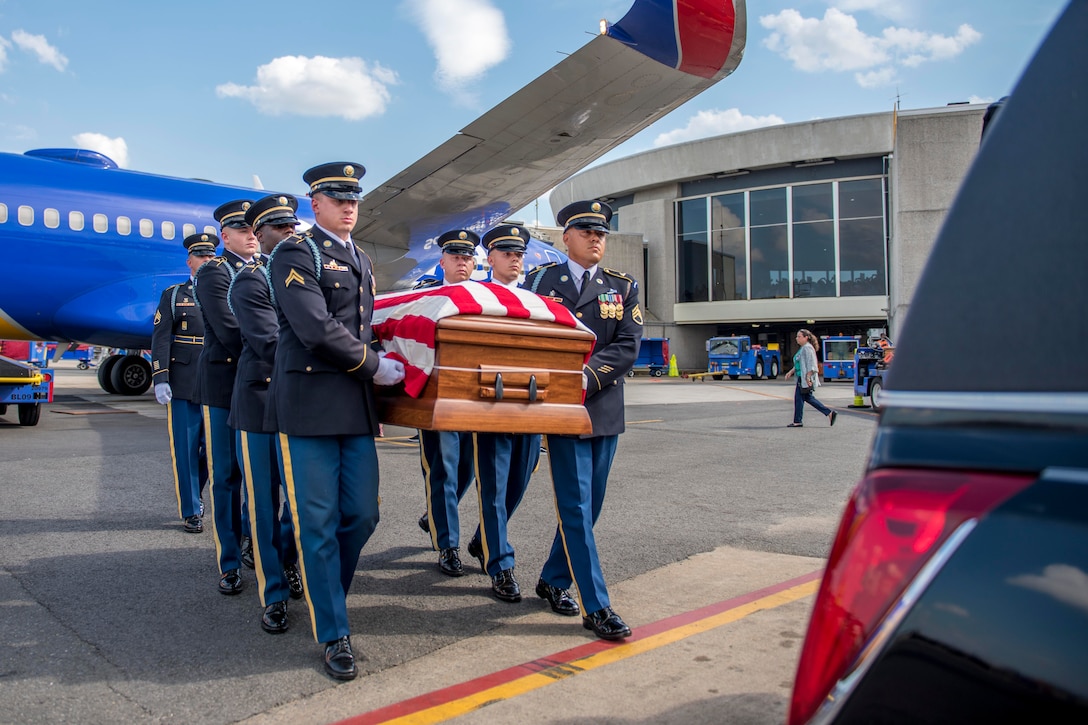 Soldiers carry a casket next to an airplane.