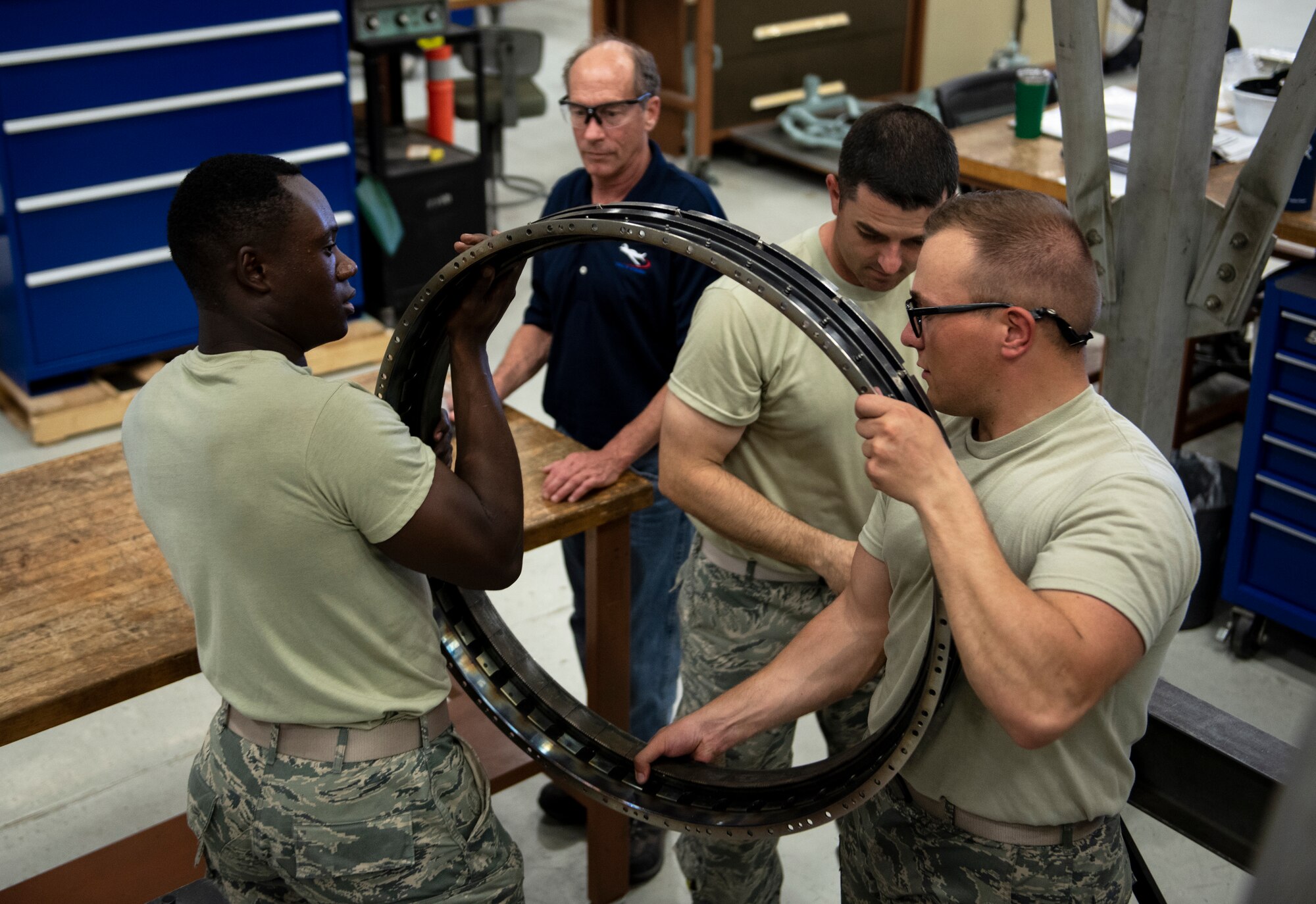 From left, Airman 1st Class Ethan Gray, Airman 1st Class Matthew Stewart and Airman Michael Chepel, 361st Training Squadron aerospace propulsion apprentice course students, carry a F110 turbine engine part while their instructor supervises at Sheppard Air Force Base, Texas, July 18, 2019. The students are tearing down a high pressure turbine and will re-install all the parts after. This process lets students understand the engine better as well as let them identify faults if the engine was assembled incorrectly. (U.S. Air Force photo by Airman 1st Class Pedro Tenorio)