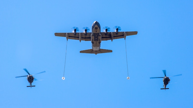 Two HH-60 Pave Hawk helicopters fly in formation with a C-130 Hercules