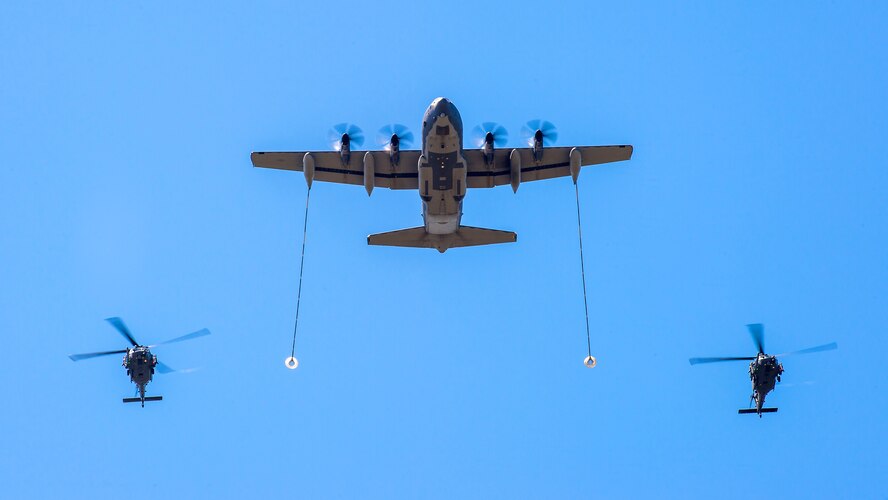 Two HH-60 Pave Hawk helicopters fly in formation with a C-130 Hercules