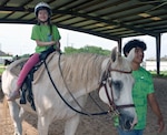 Ava Barth sits on top of a horse at the Joint Base San Antonio-Fort Sam Houston Equestrian Center June 27. Barth was one of 12 children who participated in the JBSA Exceptional Family Member Program Equestrian Camp held at the equestrian center June 25-27. The camp allowed special needs children from military families and their siblings to learn about horsemanship and to ride horses. Leading Byers on her horse is camp volunteer Antonio Nava.