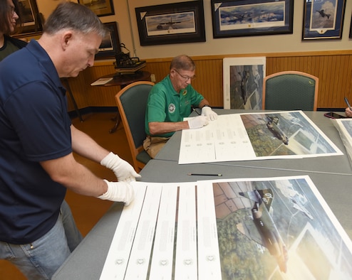 United States Air Force Aviation Artist Darby Perrin and Vietnam War Ace Col. Chuck DeBellevue carefully arrange and sign 555 copies of the piece Perrin painted for DeBellevue, entitled "Landing Denied." The piece is of a scene on Sept. 9, 1972,  when then Capt. DeBellevue and Capt. John Madden were in close proximity of a MiG 21J over Phuc Yen Airbase. (U.S. Air Force photo/Kelly White)
