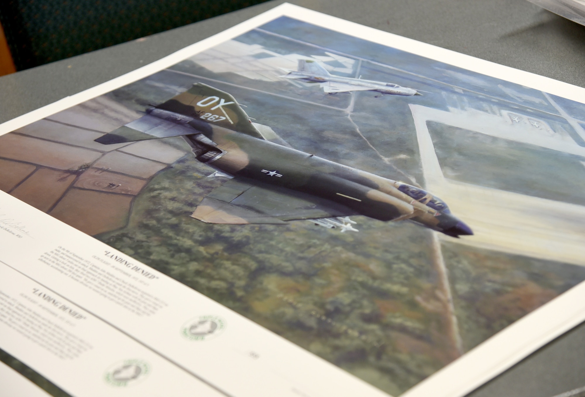 United States Air Force Aviation Artist Darby Perrin and Vietnam War Ace Col. Chuck DeBellevue carefully arrange and sign 555 copies of the piece Perrin painted for DeBellevue, entitled "Landing Denied." The piece is of a scene on Sept. 9, 1972,  when then Capt. DeBellevue and Capt. John Madden were in close proximity of a MiG 21J over Phuc Yen Airbase. (U.S. Air Force photo/Kelly White)