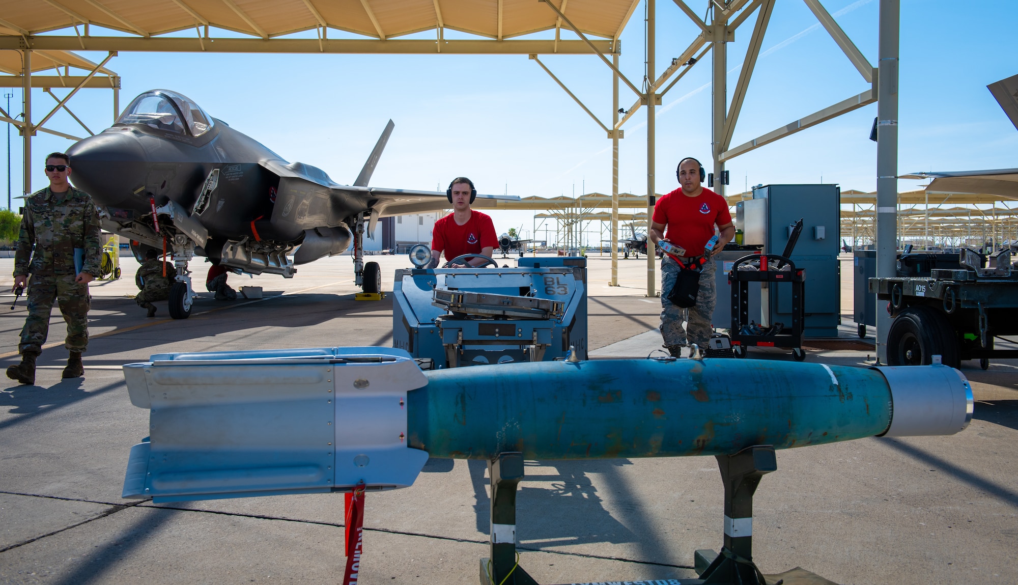 Airman 1st Class Michael Zambrano, 63rd Aircraft Maintenance Unit weapons load crew member (center), loads an inert bomb onto a jammer with his team member, Staff Sgt. Kevin McCain, 63rd AMU load crew team chief July 18, 2019, at Luke Air Force Base, Ariz.